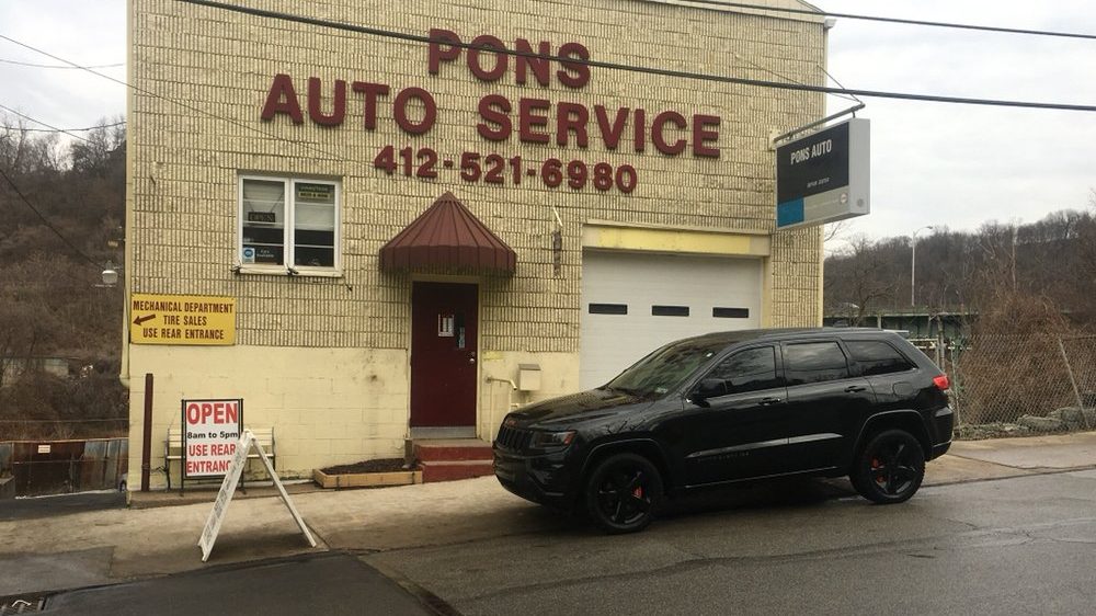 The Pons Auto Service building on Greenfield Avenue, a cream brick garage with the name and phone number in large red letters, a maroon door and awning, and a black SUV parked out front.