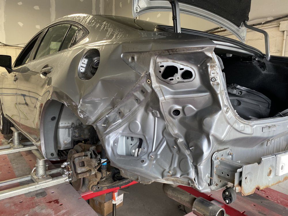 A silver car's rear quarter panel cut back to bare structure on a shop jack, trunk lid open.