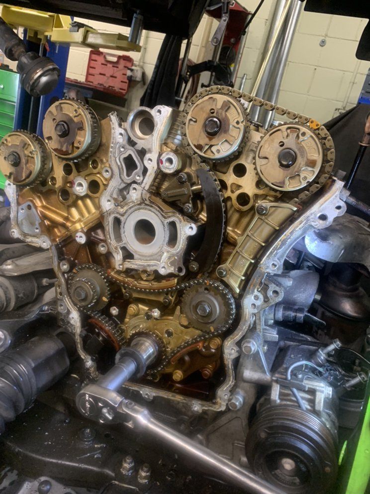 An engine with the front cover off, showing timing chains, cam gears and a socket wrench in the bay.